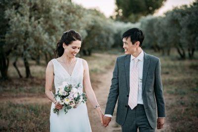 Couple de mariés souriant, main dans la main, allée d'oliviers, Château de la Beaumetane