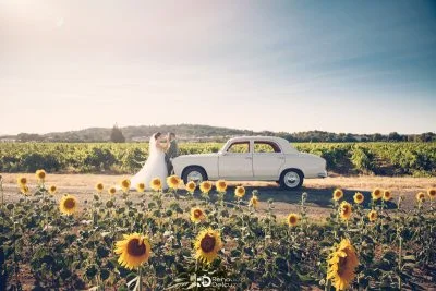 Couple de mariés posant près d'une voiture ancienne entourés de tournesols, Château Beauchene