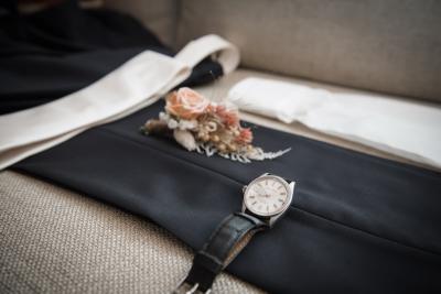Montre élégante et petite fleur rose sur veste noire, préparatifs de mariage Bastide Saint Julien